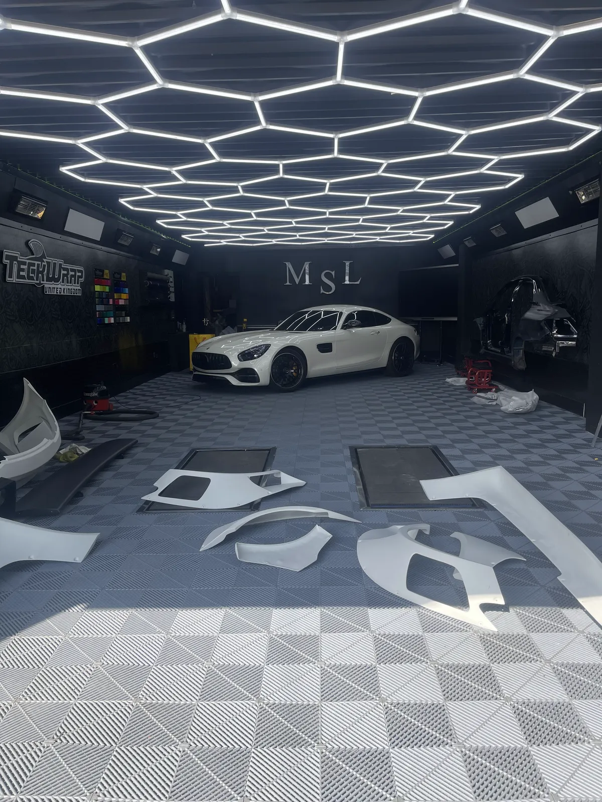 Widebody panels laid out unpainted on the workshop floor beside the AMG GT