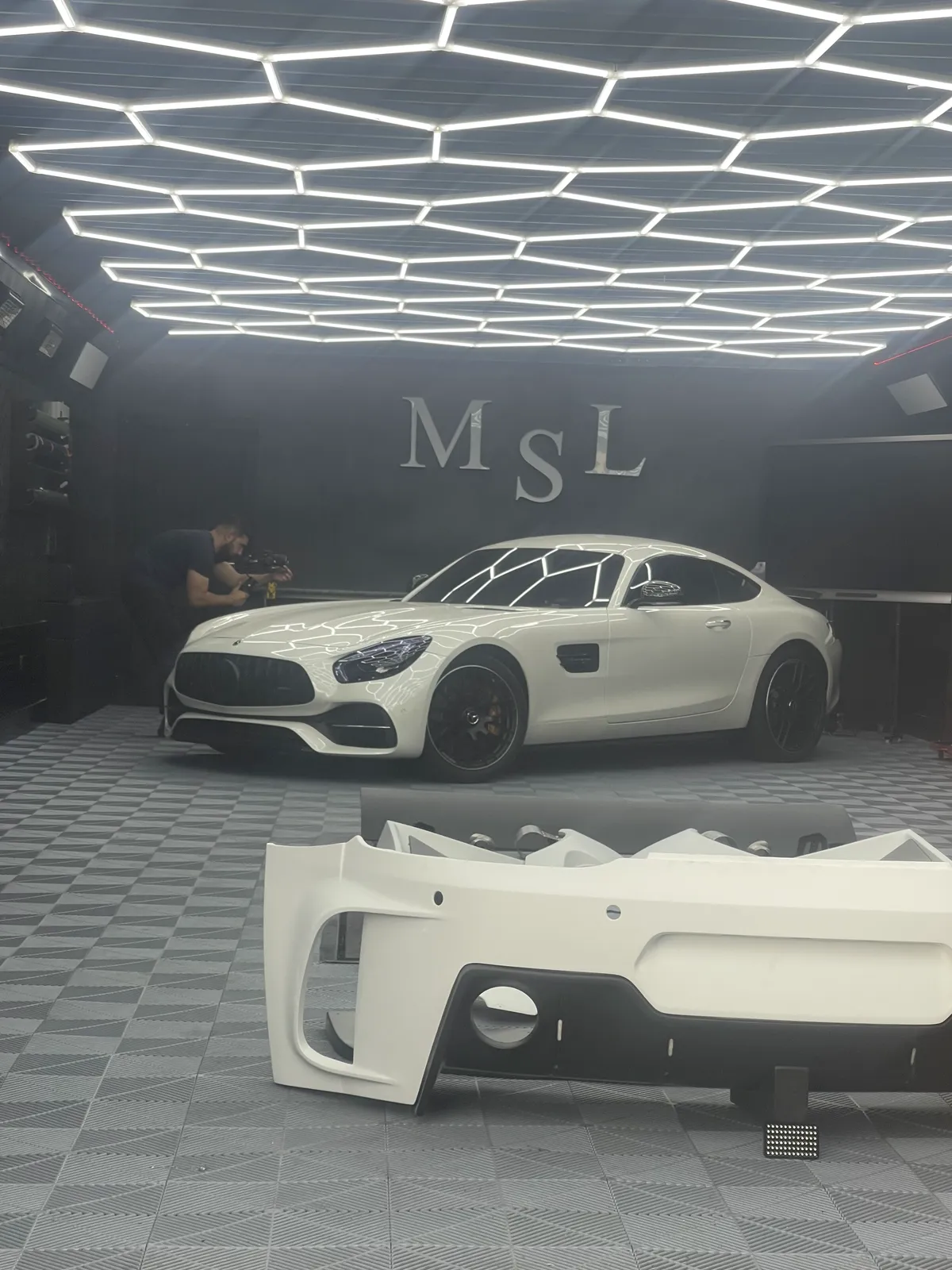 An unpainted widebody front bumper in the foreground with the AMG GT behind