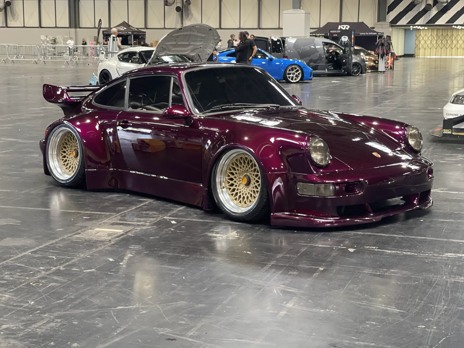 The finished widebody Porsche 911 in aubergine metallic on gold BBS wheels at a car show